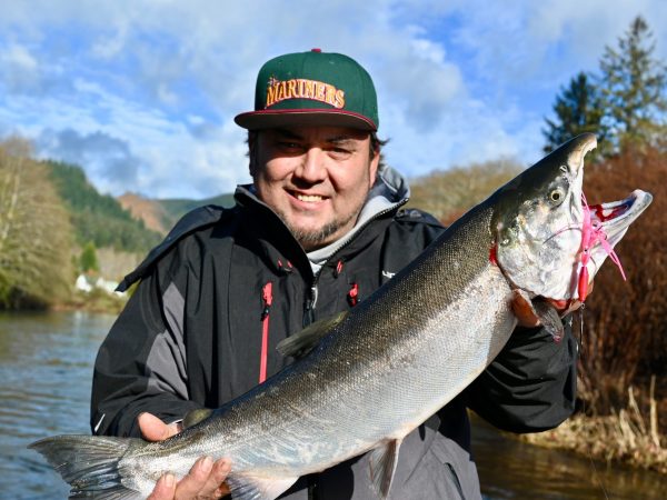 Person holding a large fish by a river under a blue sky.