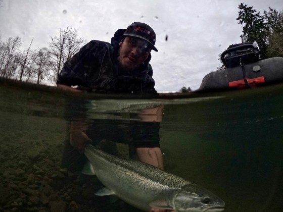 Man holding a fish in a river, viewed above and below water.
