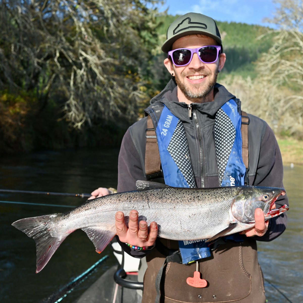Person in sunglasses and cap holds a large fish on a boat with trees in the background.