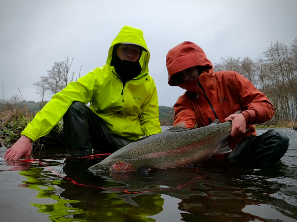 Two people in rain jackets holding a large fish over a shallow body of water.