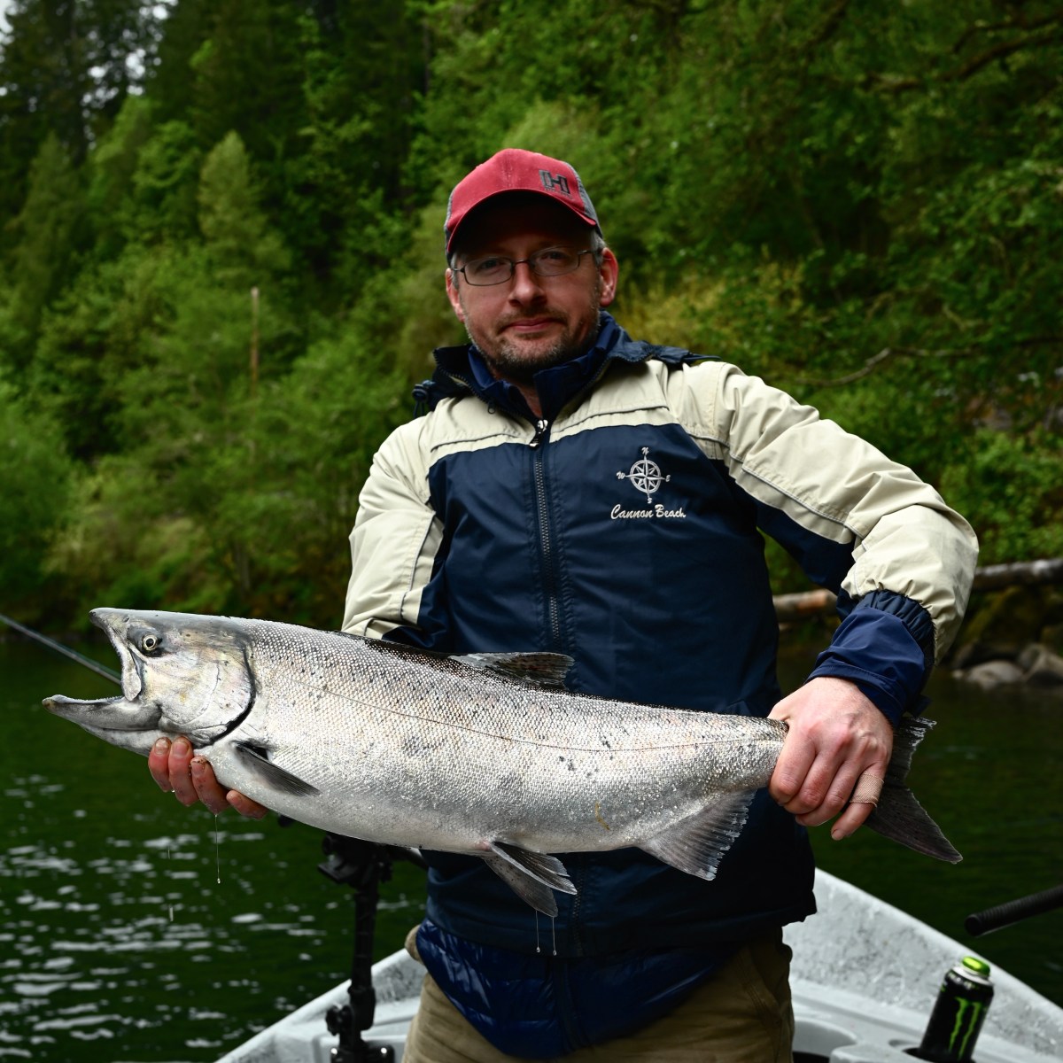 Person holding a large fish on a boat with a forest backdrop.
