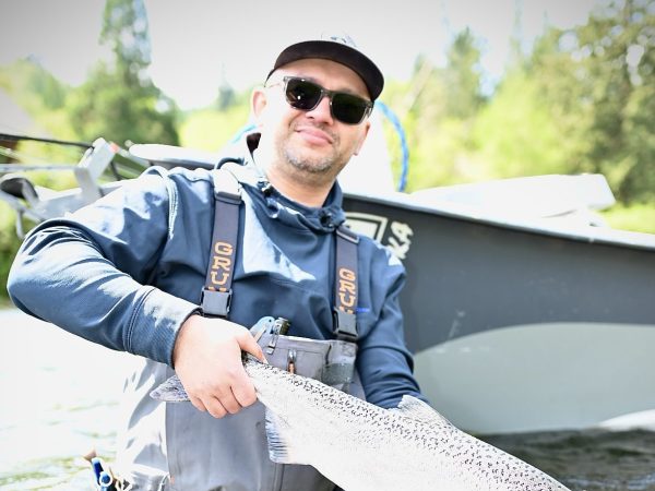 Man in sunglasses holds a large fish while standing in a river.