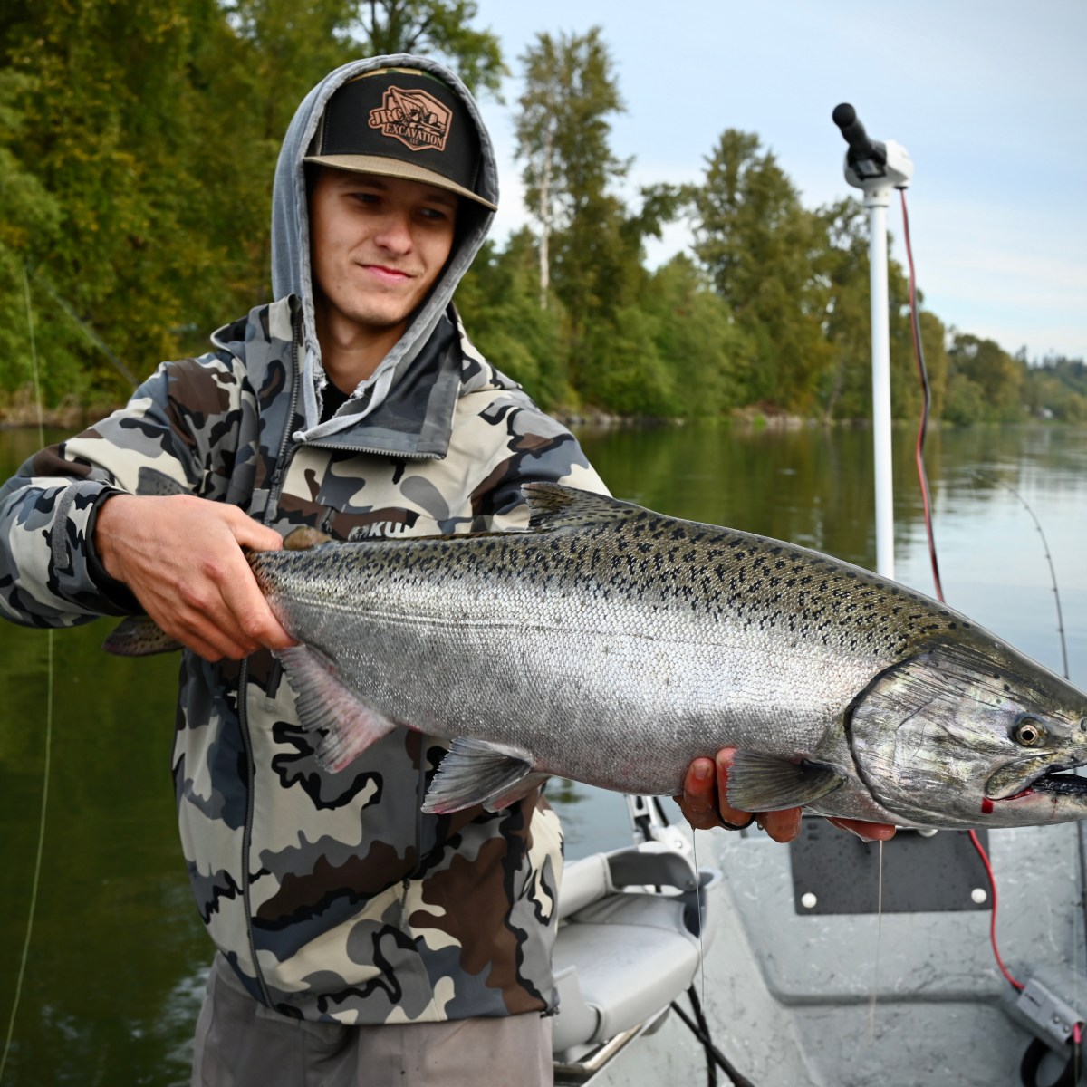 Person on a boat holding a large fish with water and trees in the background.