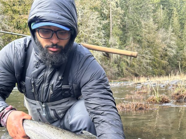 Person in waterproof gear holding a large fish in a river with forested background.