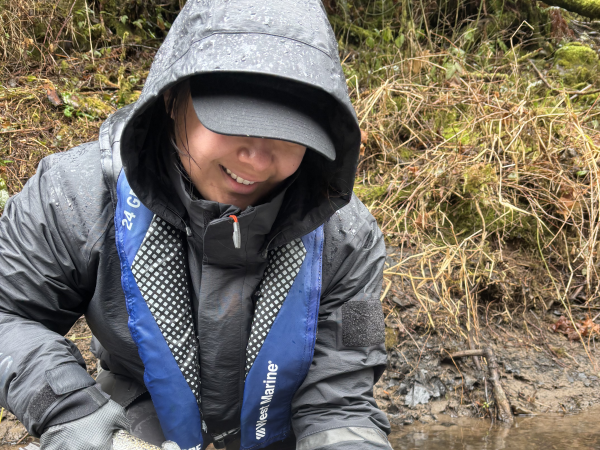 Person in rain gear holding a large fish near a muddy riverbank.