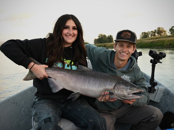 Two people sitting on a boat holding a large fish, smiling.