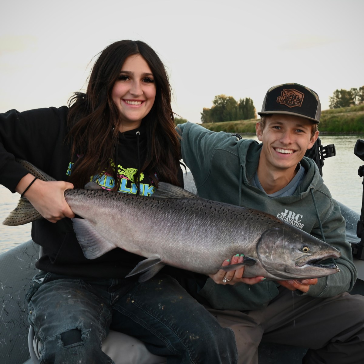 Two people sitting on a boat holding a large fish, smiling.