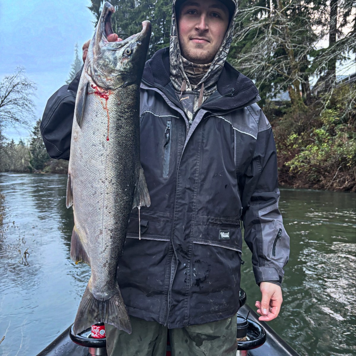 Person holding a large fish on a boat in a river surrounded by trees.