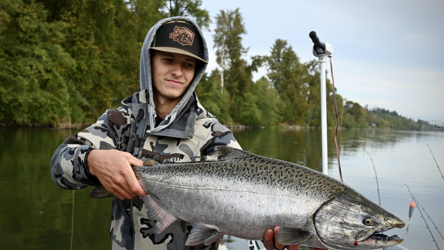 Person on boat holding a large fish with trees in the background.