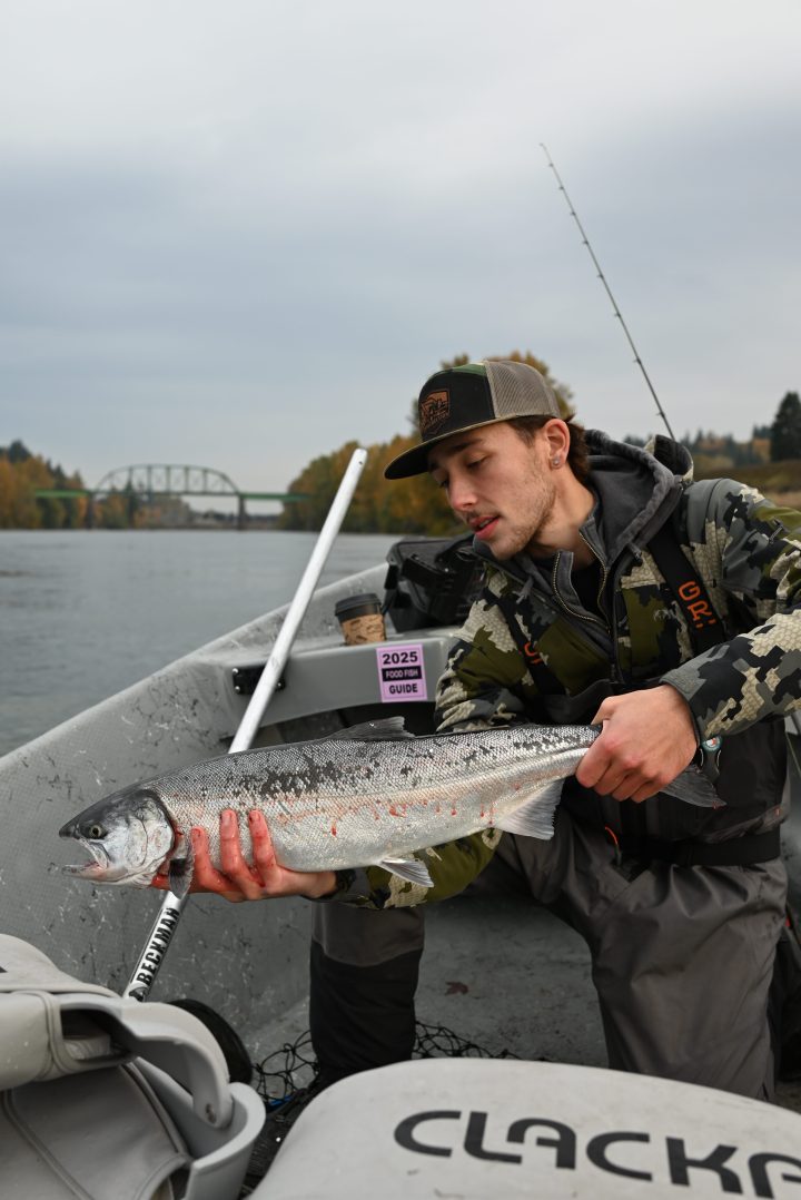 Person in a boat holding a fish, with a river and bridge in the background.