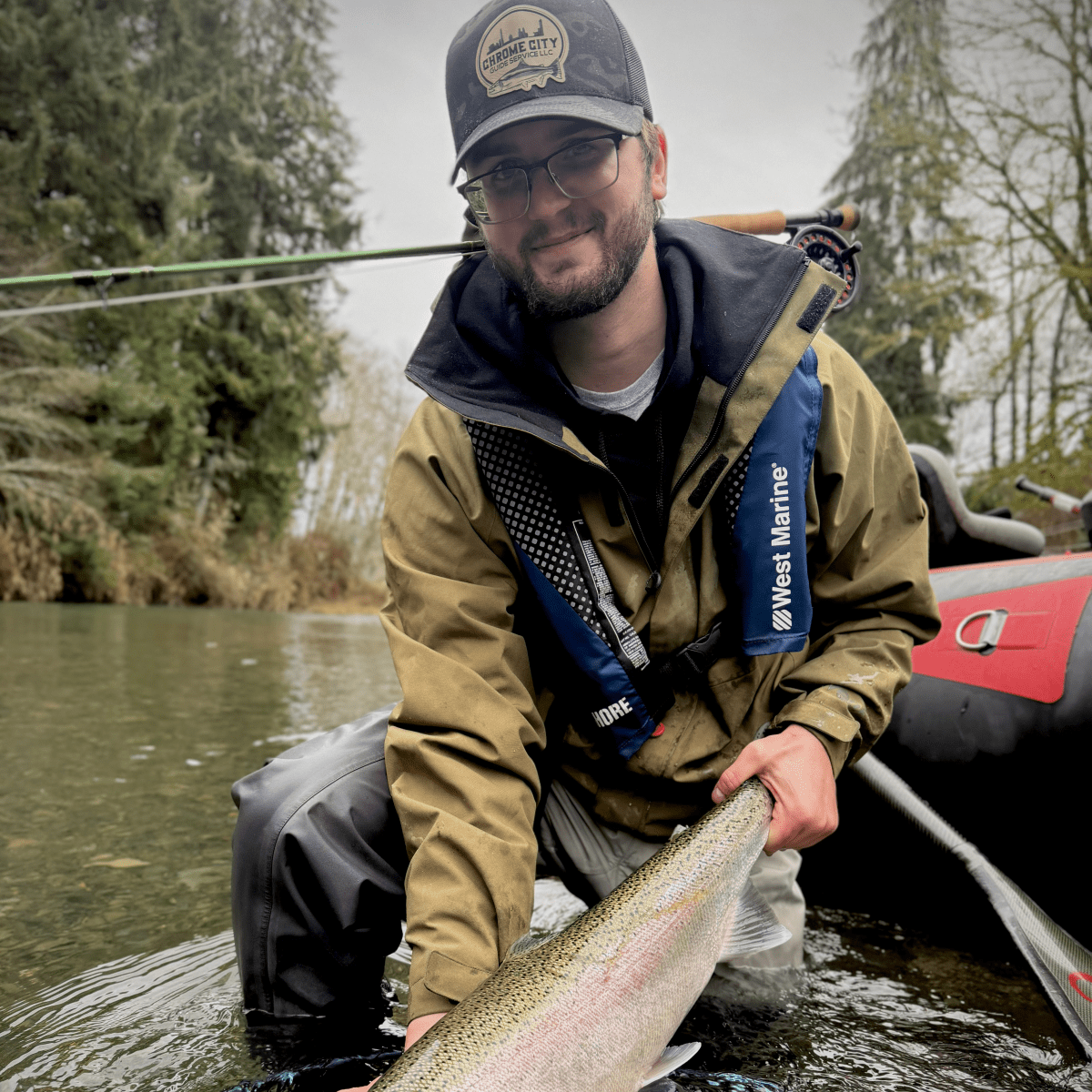 Person in jacket and cap holding a large fish in a river.