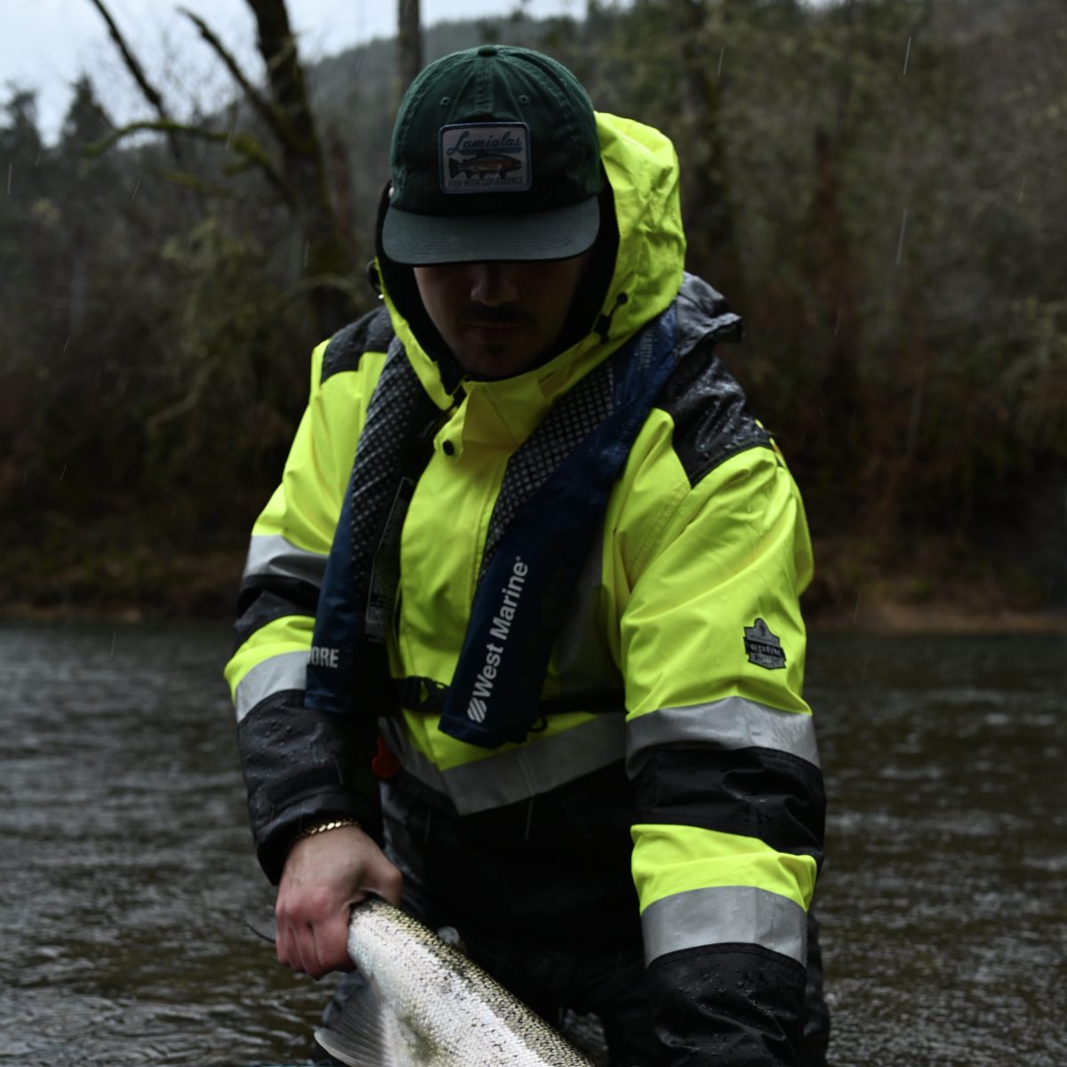 Person in rain gear holds a large fish over a river's water surface.